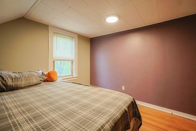 bedroom with wood finished floors, baseboards, and vaulted ceiling