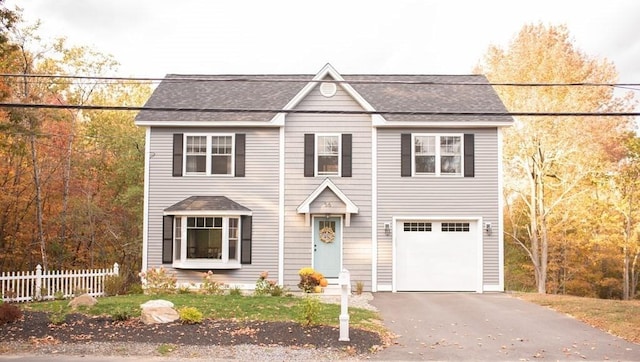 view of front facade with an attached garage, roof with shingles, fence, and driveway