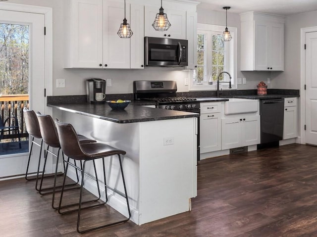 kitchen with dark countertops, a sink, dishwasher, a peninsula, and stainless steel microwave