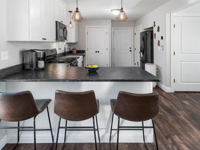 kitchen with stainless steel range with gas stovetop, a peninsula, dark countertops, and freestanding refrigerator
