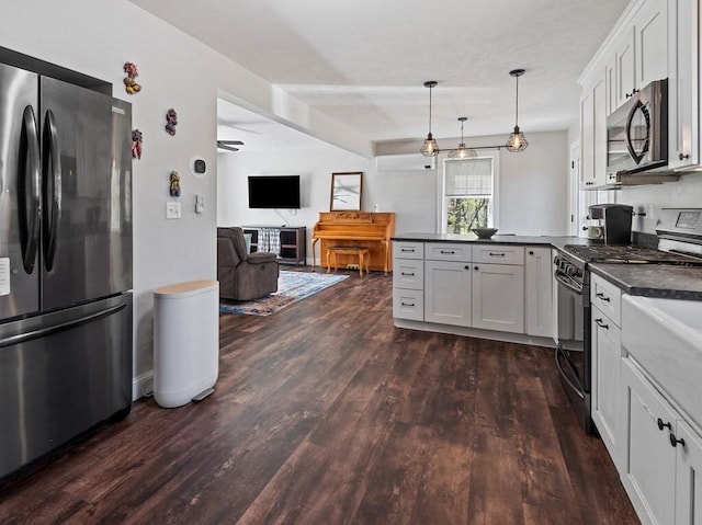 kitchen featuring dark countertops, appliances with stainless steel finishes, a peninsula, open floor plan, and dark wood-type flooring