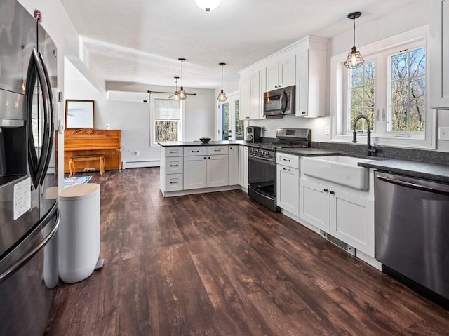 kitchen featuring a peninsula, dark countertops, dark wood-type flooring, a sink, and appliances with stainless steel finishes