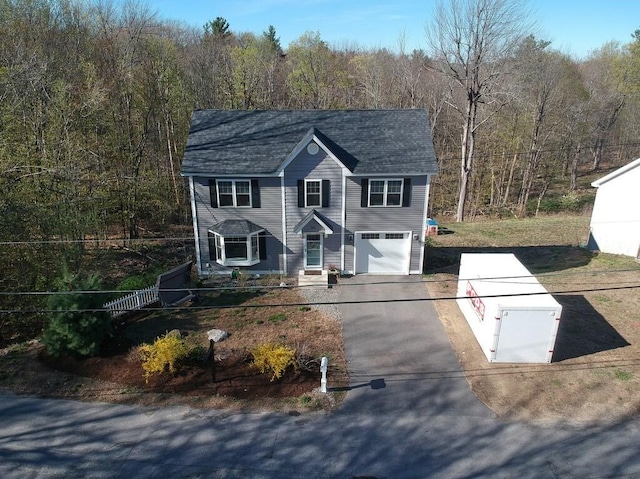 view of front of house featuring an attached garage, driveway, a wooded view, and a shingled roof