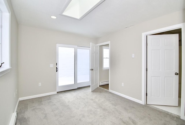 carpeted empty room featuring a skylight and a baseboard heating unit