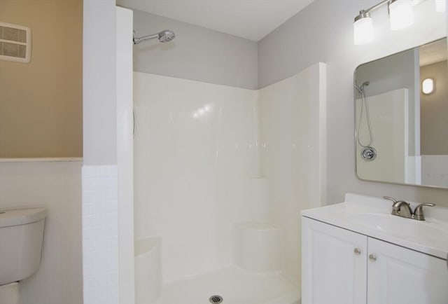 bathroom with a shower, tile walls, vanity, and toilet