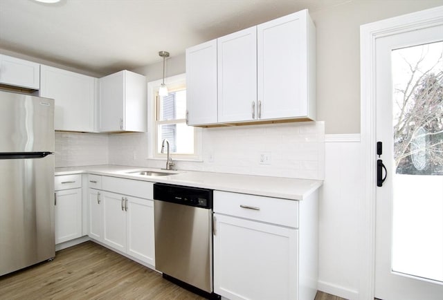 kitchen with stainless steel appliances, white cabinetry, sink, and decorative light fixtures