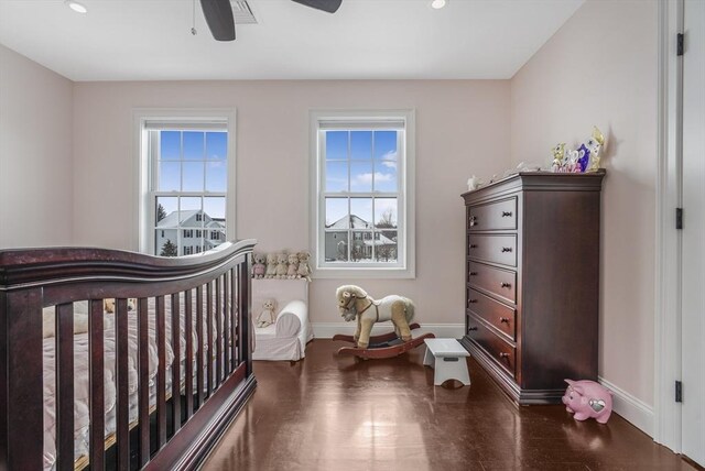 bedroom featuring ceiling fan, multiple windows, and a nursery area