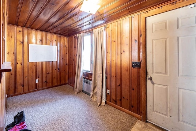 carpeted empty room with radiator, wood ceiling, and wooden walls