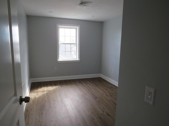 spare room featuring wood finished floors, visible vents, and baseboards