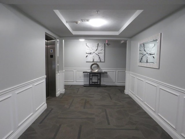 hall featuring visible vents, dark carpet, elevator, a decorative wall, and a raised ceiling