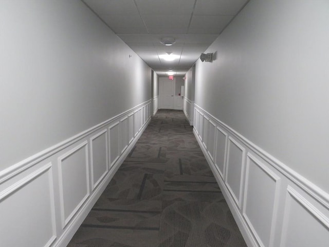 corridor featuring a drop ceiling, carpet, a wainscoted wall, and a decorative wall