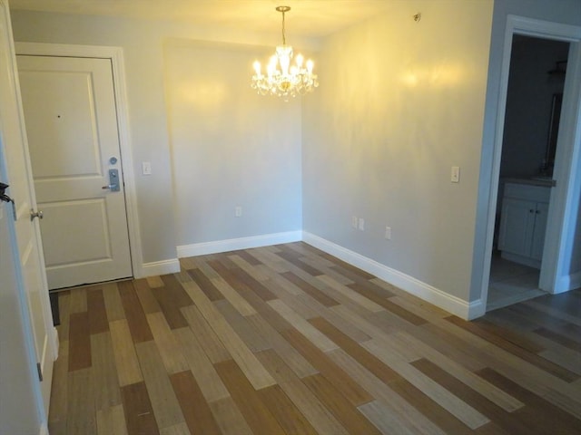 unfurnished room featuring a notable chandelier, baseboards, and wood finished floors