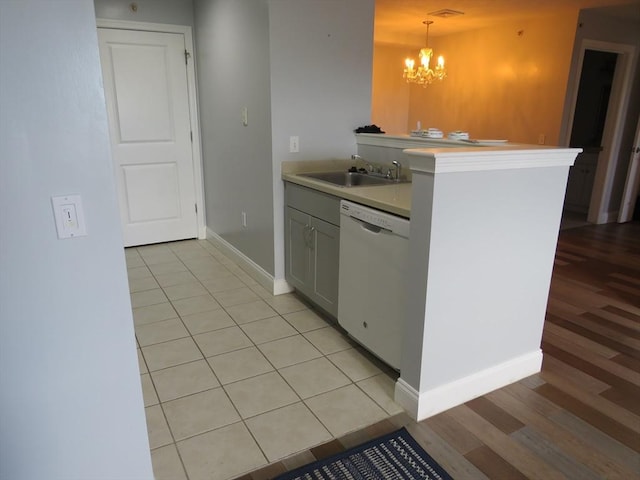 kitchen featuring baseboards, white dishwasher, a sink, light countertops, and pendant lighting