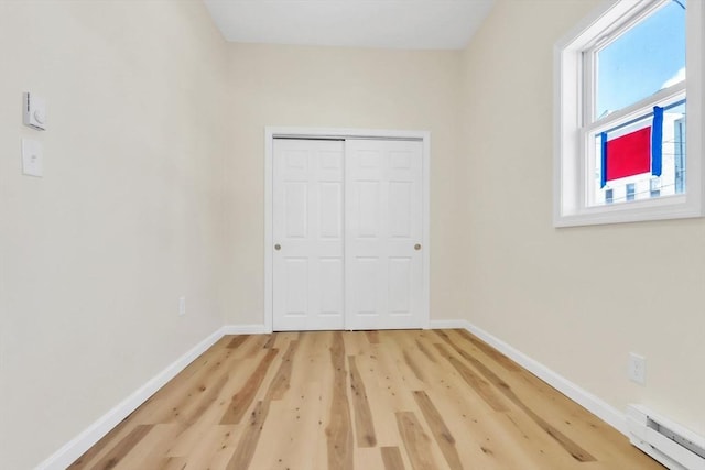 unfurnished bedroom with a closet, baseboards, baseboard heating, and light wood-type flooring