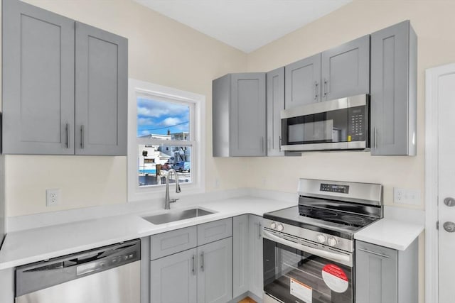 kitchen with gray cabinetry, stainless steel appliances, light countertops, and a sink