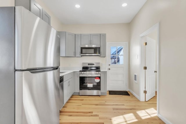 kitchen featuring light wood finished floors, light countertops, recessed lighting, gray cabinets, and stainless steel appliances