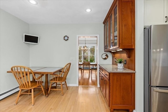 kitchen featuring freestanding refrigerator, brown cabinets, baseboard heating, and light wood finished floors