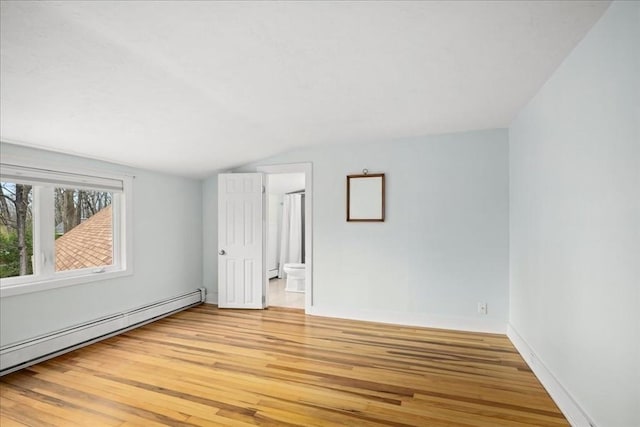 spare room featuring baseboard heating, lofted ceiling, and light wood-style floors