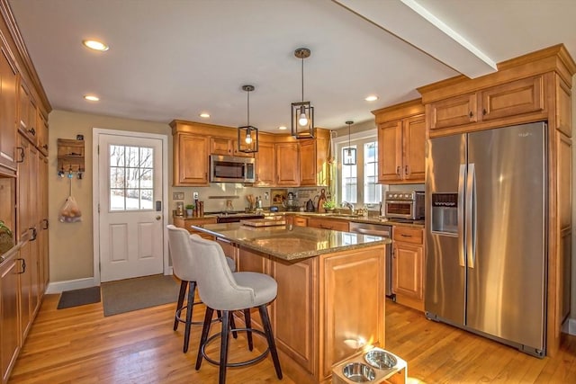 kitchen with appliances with stainless steel finishes, sink, dark stone counters, hanging light fixtures, and a center island