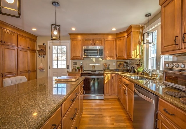 kitchen with hanging light fixtures, appliances with stainless steel finishes, sink, and dark stone counters