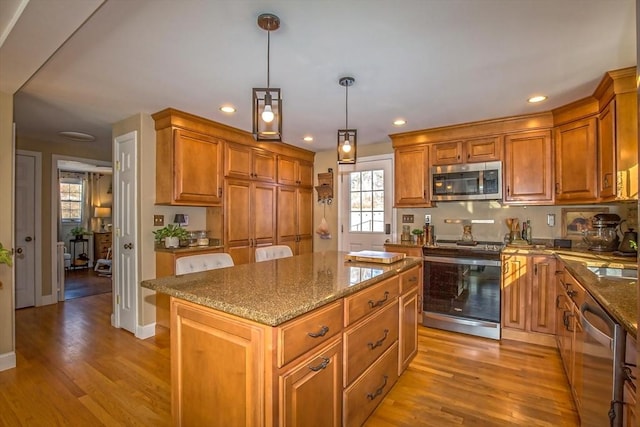 kitchen with stainless steel appliances, hanging light fixtures, a center island, and light hardwood / wood-style flooring