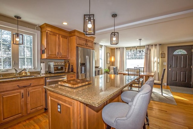 kitchen with sink, appliances with stainless steel finishes, a center island, decorative light fixtures, and light wood-type flooring