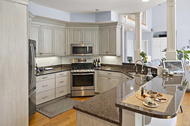 kitchen featuring sink, appliances with stainless steel finishes, ornate columns, kitchen peninsula, and light wood-type flooring