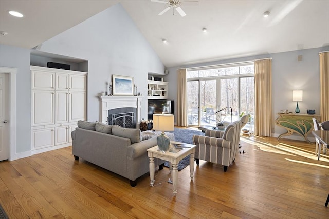 living room featuring a tile fireplace, ceiling fan, high vaulted ceiling, and light hardwood / wood-style flooring