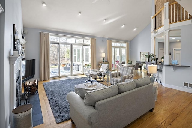 living room with light hardwood / wood-style flooring, high vaulted ceiling, and ornate columns