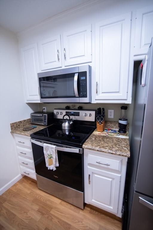1610 Franklin Crossing Rd Unit 1610, Franklin, MA 02038 - kitchen featuring stainless steel appliances, light wood-style flooring, white cabinets, ornamental molding, and light stone countertops