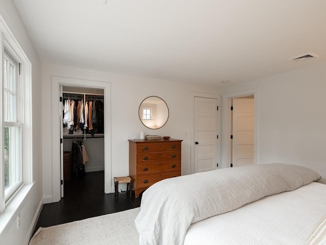 bedroom with dark wood finished floors, a walk in closet, visible vents, and a closet