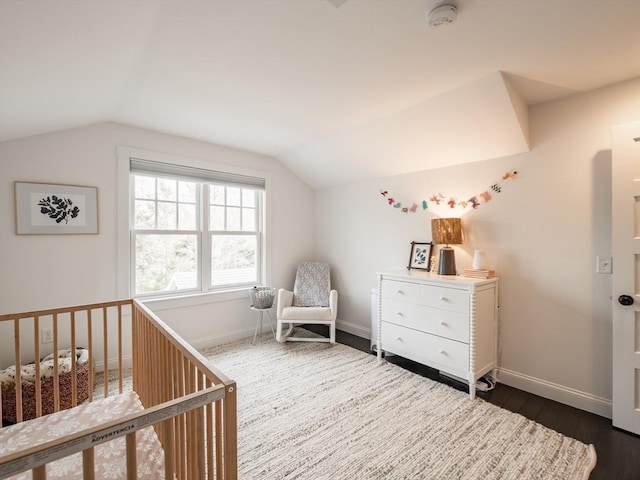 bedroom featuring dark wood finished floors, a nursery area, baseboards, and vaulted ceiling