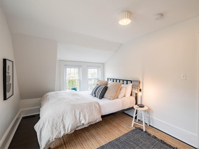 bedroom with baseboards, lofted ceiling, visible vents, and wood finished floors