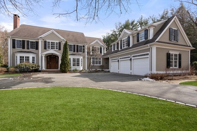 view of front facade featuring a garage, a front lawn, a chimney, and driveway