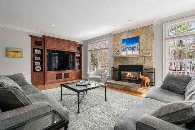 living area featuring light wood finished floors, a healthy amount of sunlight, a fireplace, and crown molding