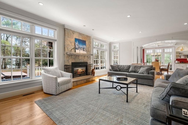 living area with visible vents, a stone fireplace, crown molding, and wood finished floors