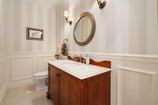 half bath featuring a decorative wall, vanity, wainscoting, and wallpapered walls