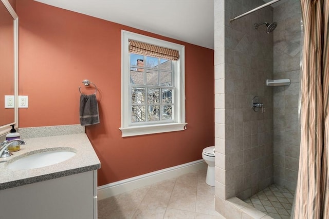 bathroom with tile patterned floors, toilet, a tile shower, baseboards, and vanity