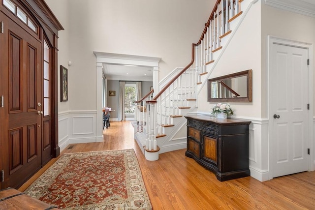 foyer with stairway, light wood-style floors, a high ceiling, crown molding, and a decorative wall