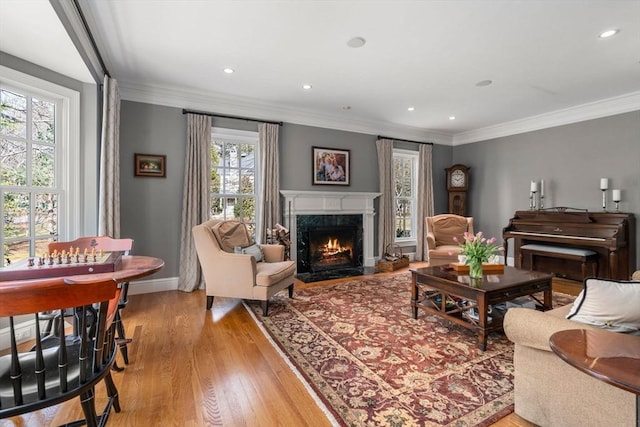 living area with baseboards, recessed lighting, a fireplace, ornamental molding, and light wood-style floors