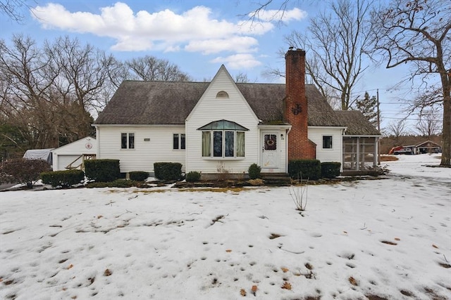 snow covered property with a detached garage, an outdoor structure, a sunroom, and a chimney