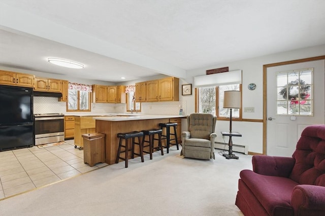 kitchen featuring stainless steel electric stove, freestanding refrigerator, light countertops, under cabinet range hood, and open floor plan