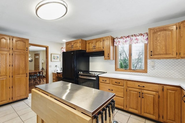 kitchen with light tile patterned flooring, freestanding refrigerator, electric stove, under cabinet range hood, and backsplash