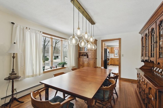 dining area with a baseboard heating unit, light wood-style floors, baseboards, and a textured ceiling