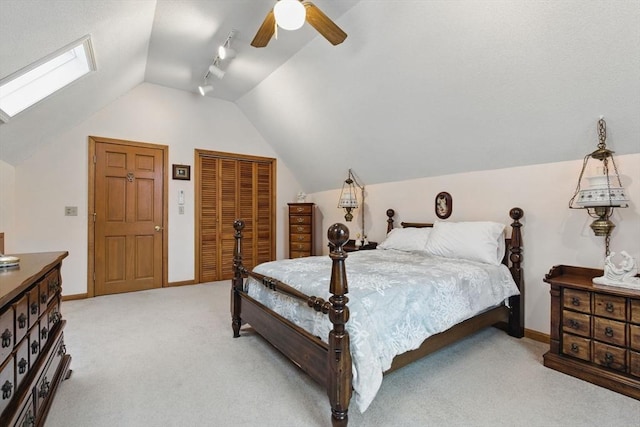 bedroom featuring baseboards, lofted ceiling with skylight, light carpet, a closet, and a ceiling fan