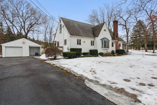 view of home's exterior featuring a shingled roof, a detached garage, aphalt driveway, a chimney, and an outdoor structure