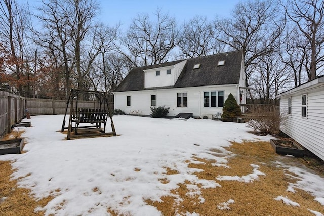 snow covered back of property with a shingled roof and fence