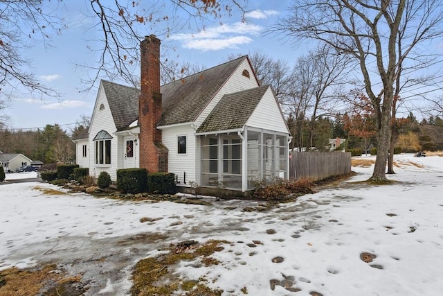 snow covered property with a chimney, fence, and a sunroom