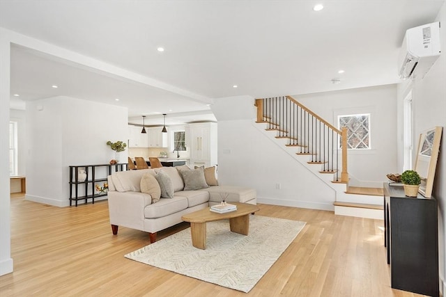 living room featuring baseboards, a wall mounted air conditioner, stairway, and light wood finished floors