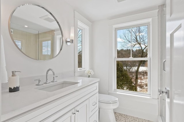 bathroom with toilet, plenty of natural light, vanity, and speckled floor